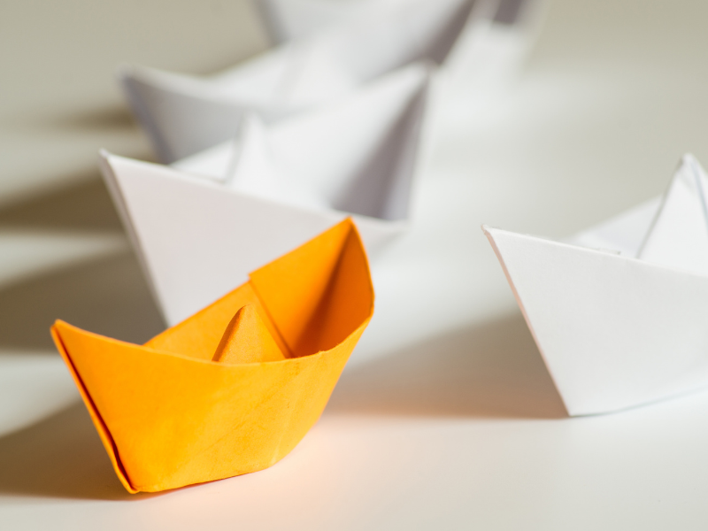 Oranges Papierschiff hebt sich von weißen ab – Employer Page Konzept und Arbeitgeberpositionierung mit arthus Personalberatung Wien